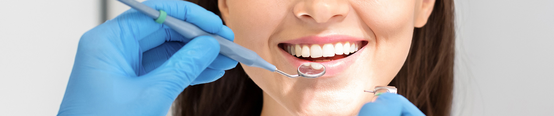 A person is seated in a dental chair, receiving care from a dental professional who stands behind them.